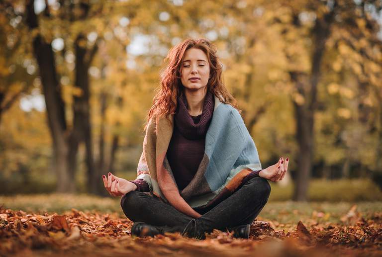 En kvinna som sitter i en meditationsställning i en skog.