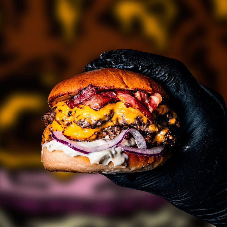 Restauranger i Stockholm. En hand håller upp en burgare med ost och bacon på Bastard Burgers.