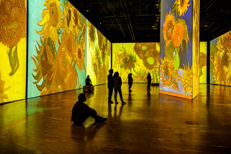 Besökare i en utställningshall med Van Goghs målningar projicerade på väggarna