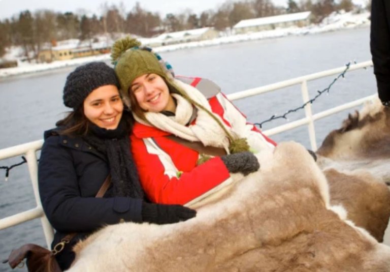 Två människor i vinterkläder som ler mot kameran. De sitter på en båt, och i bakgrunden kan man se vatten och ett snöigt Stockholm.