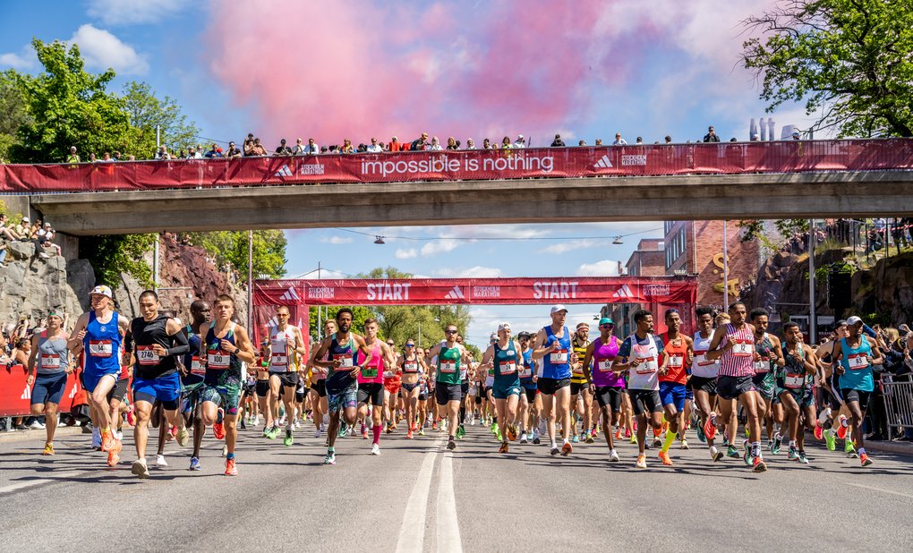 Löpare startar ett maraton en solig dag och passerar under en bro med en röd banderoll som säger ”Impossible is nothing.”
