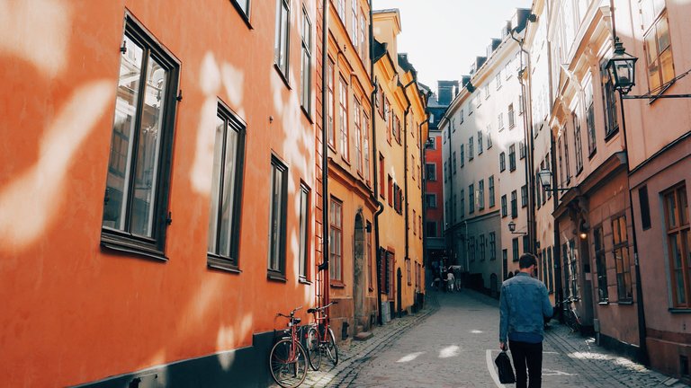 Vår i Stockholm. En ung man går längs med kullerstenarna på en gata i Gamla Stan. På båda sidor av honom syns gamla hus.