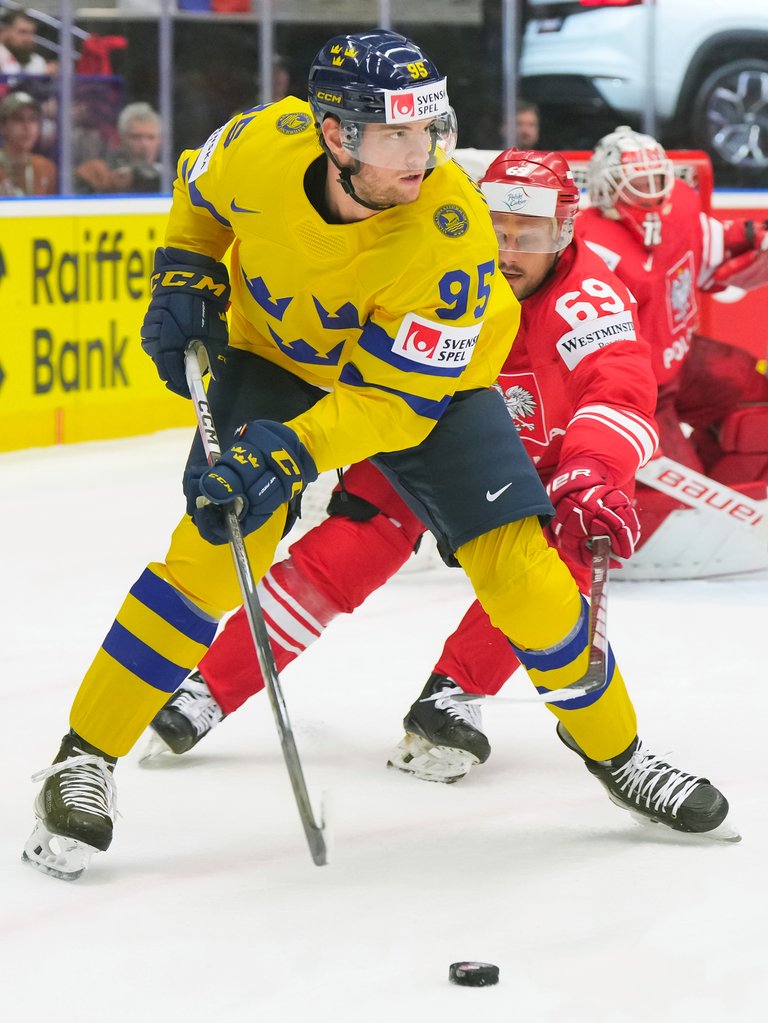 Hockeyspelare under match. EN svensk spelare driver pucken på isen. Bakom honom ser man en österrikisk spelare närma sig.