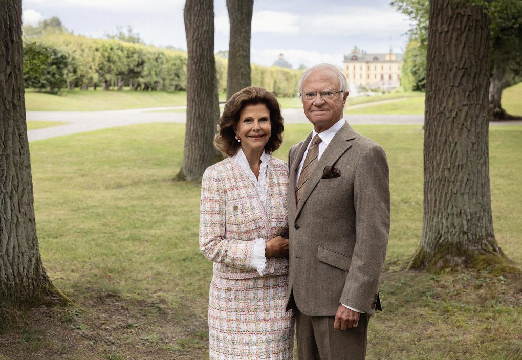 Kungaparet står tillsammans i en park med träd och ett slott i bakgrunden.
