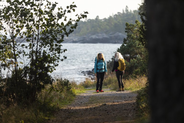 Two women standing on a walking trail, with the ocean as background, along Roslagsleden.